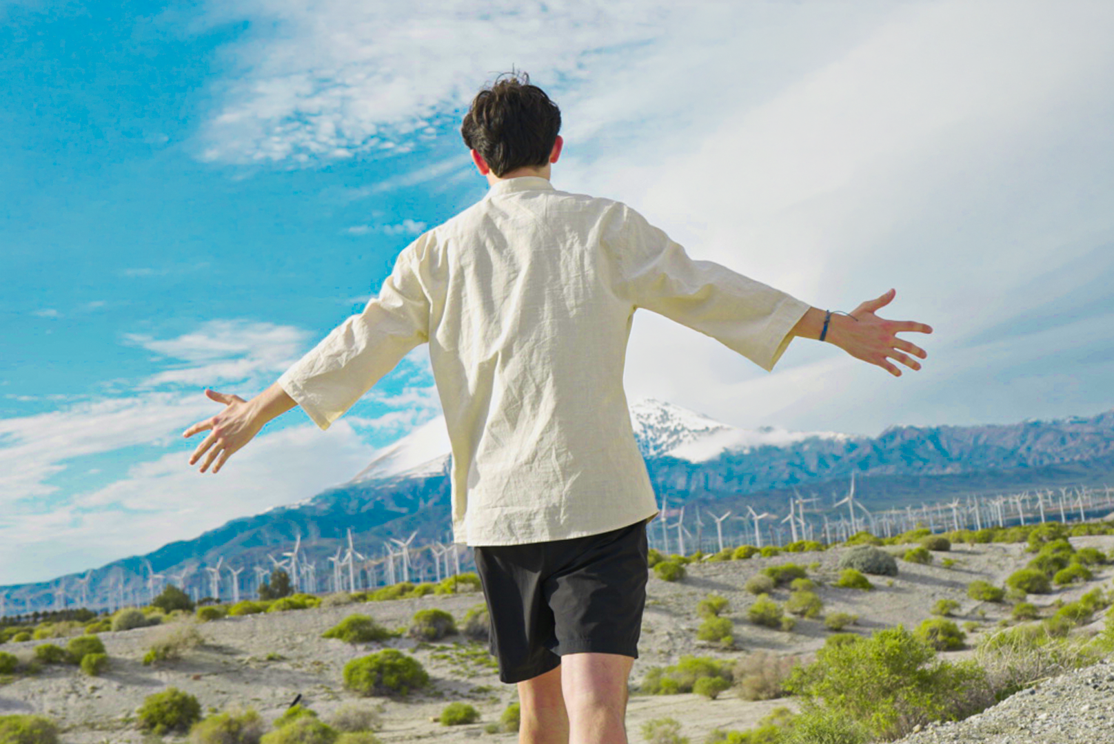 James Brewster standing arms-wide in a desert wind farm